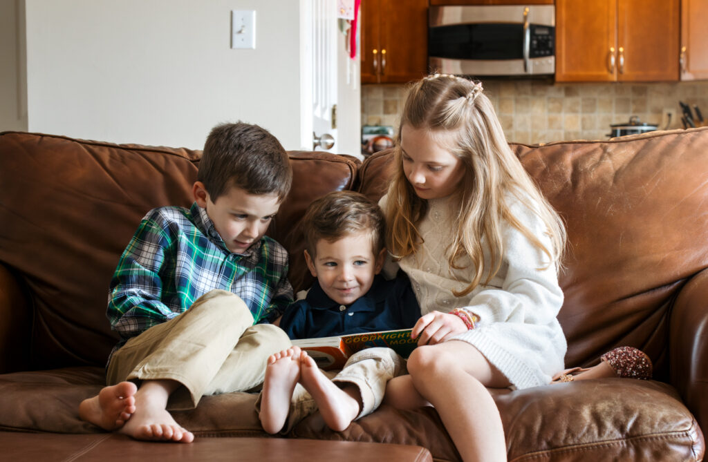 Three children reading a book in their home