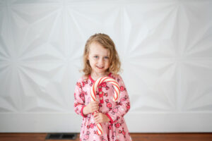little girl holding a giant candy cane in front of a white wall