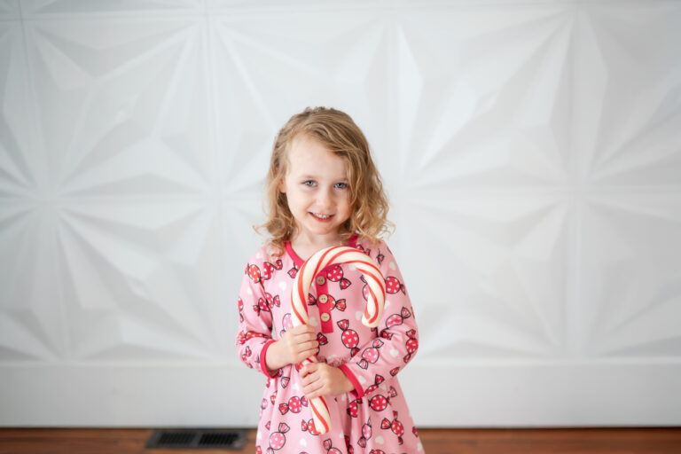 little girl holding a giant candy cane in front of a white wall