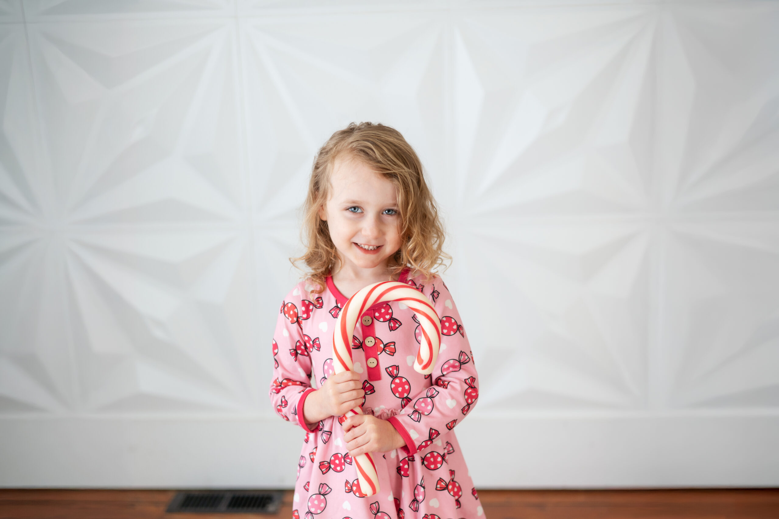 little girl holding a giant candy cane in front of a white wall