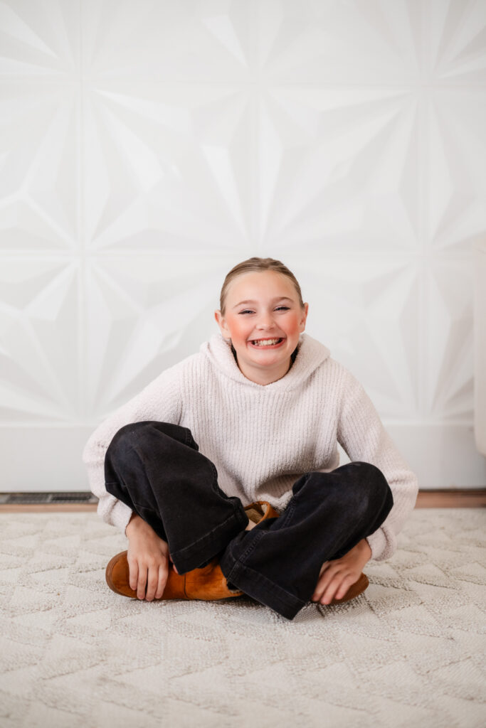 girl smiling brightly sitting criss cross on the floor